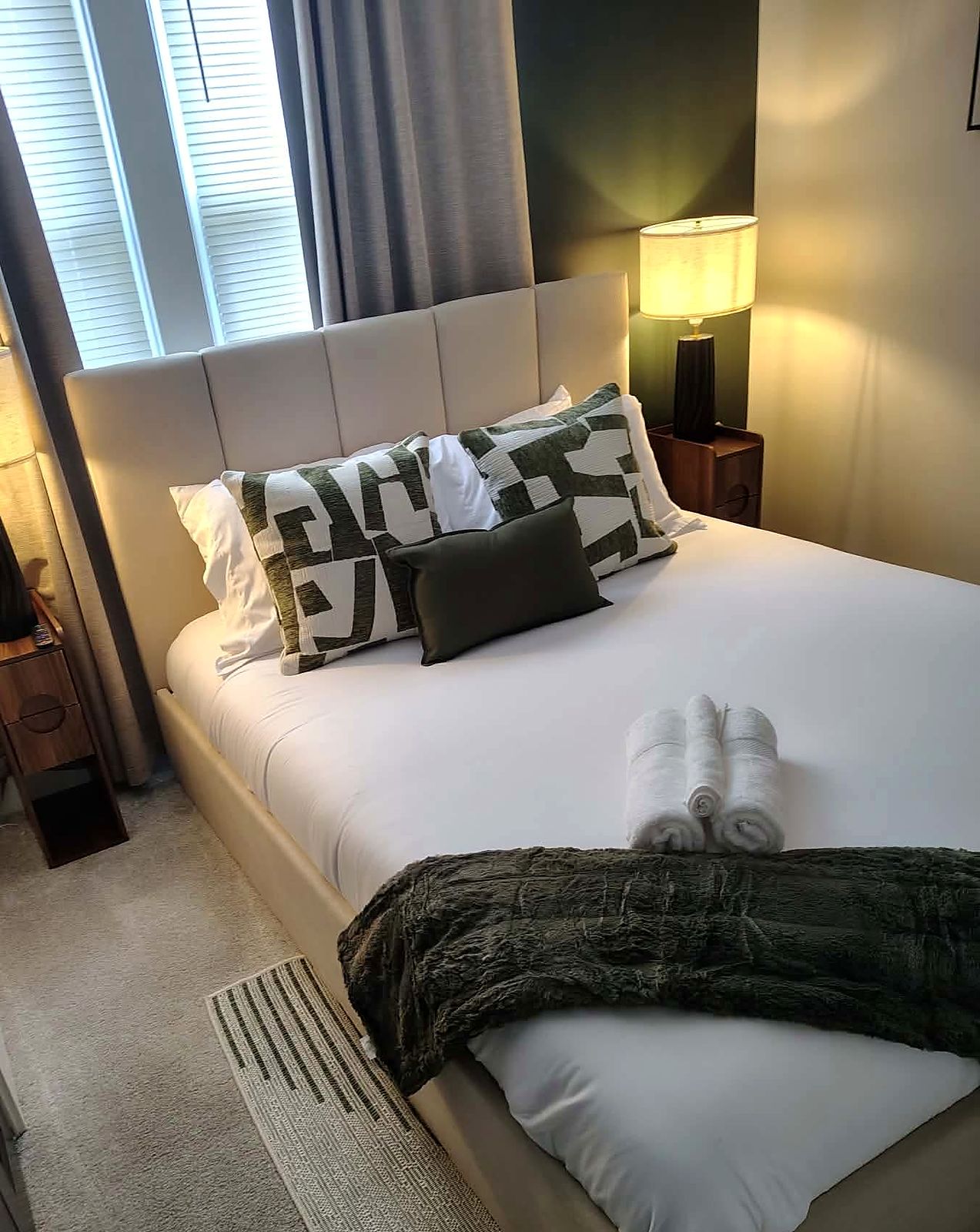 Made bed with rolled towels, patterned pillows and warm bedside lamps