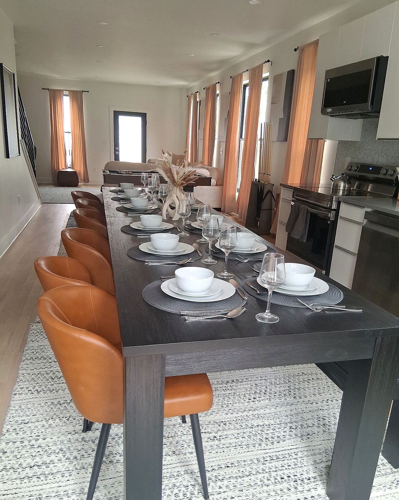 Long dining table set with white dishes, glassware and cognac leather chairs in a short-term rental