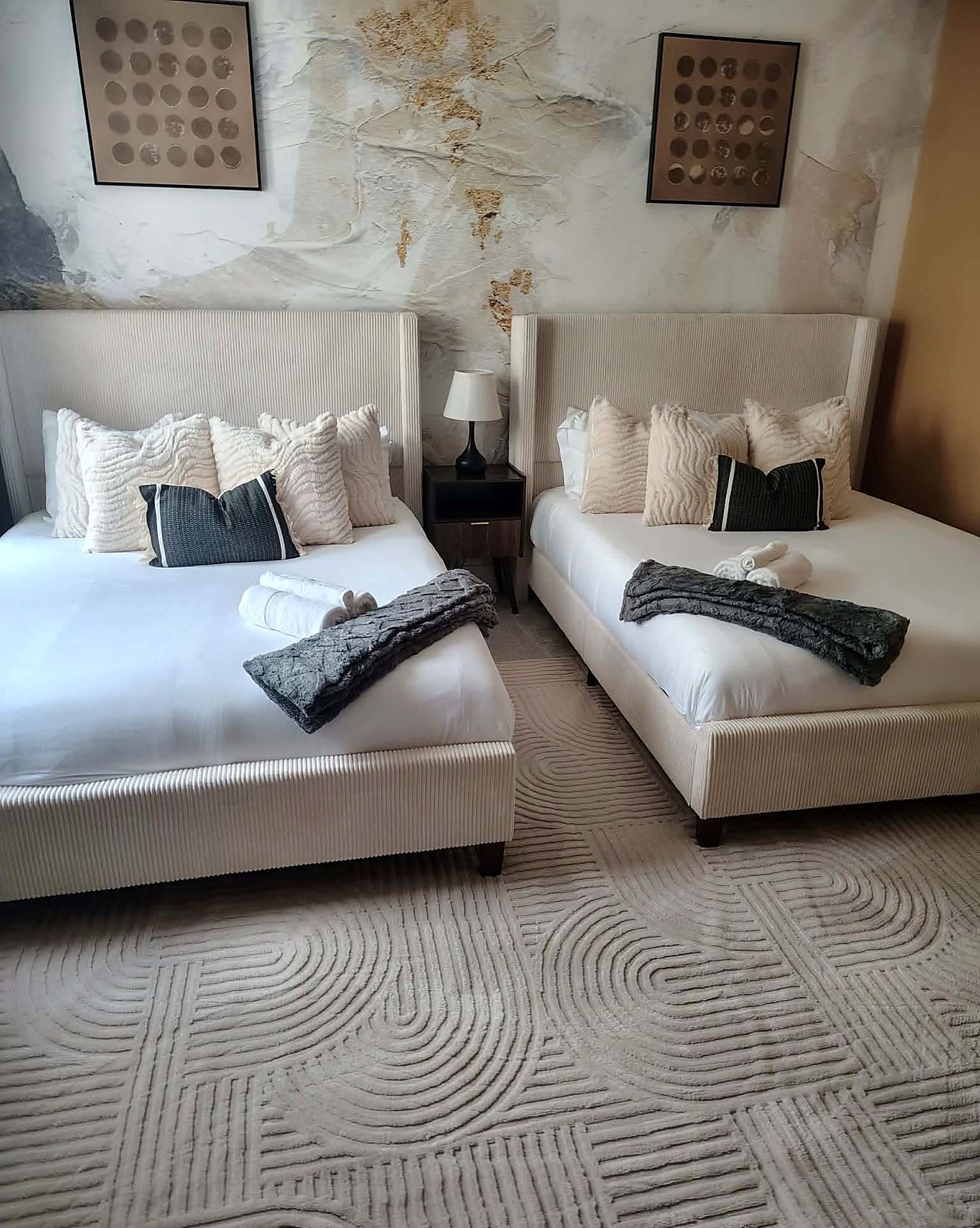 Two crisply made queen beds with rolled towels and throws over a textured rug